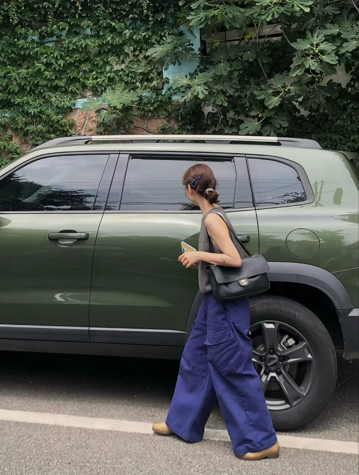 Black flap shoulder bag worn with a charcoal sleeveless top, blue-violet wide-leg trousers and tan shoes