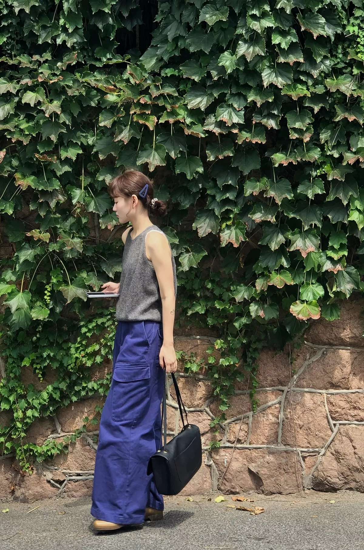 Side view of a black shoulder bag held beside blue-violet wide-leg cargo trousers