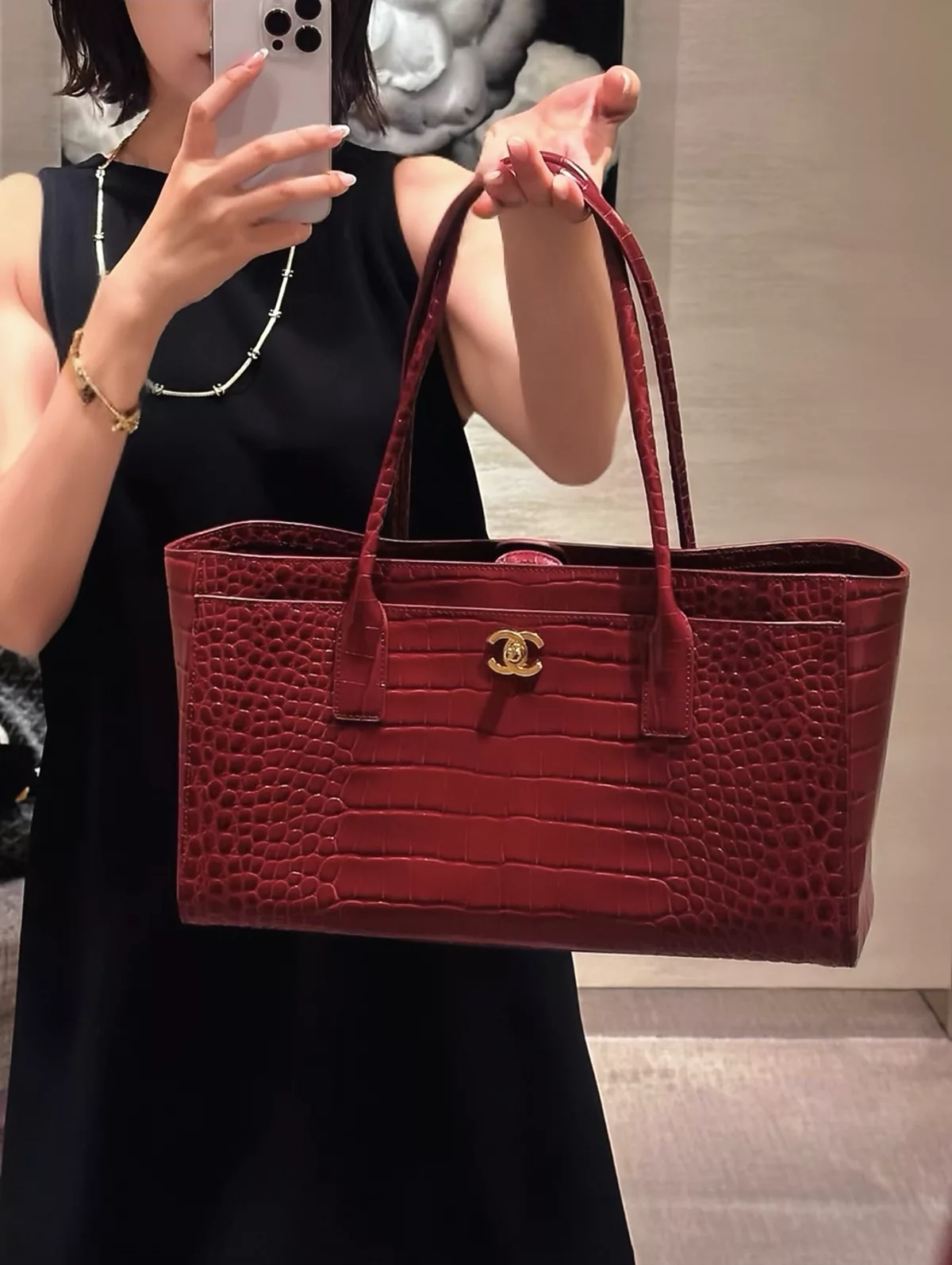 Burgundy textured tote carried with a black sleeveless outfit and a fine gold-coloured necklace